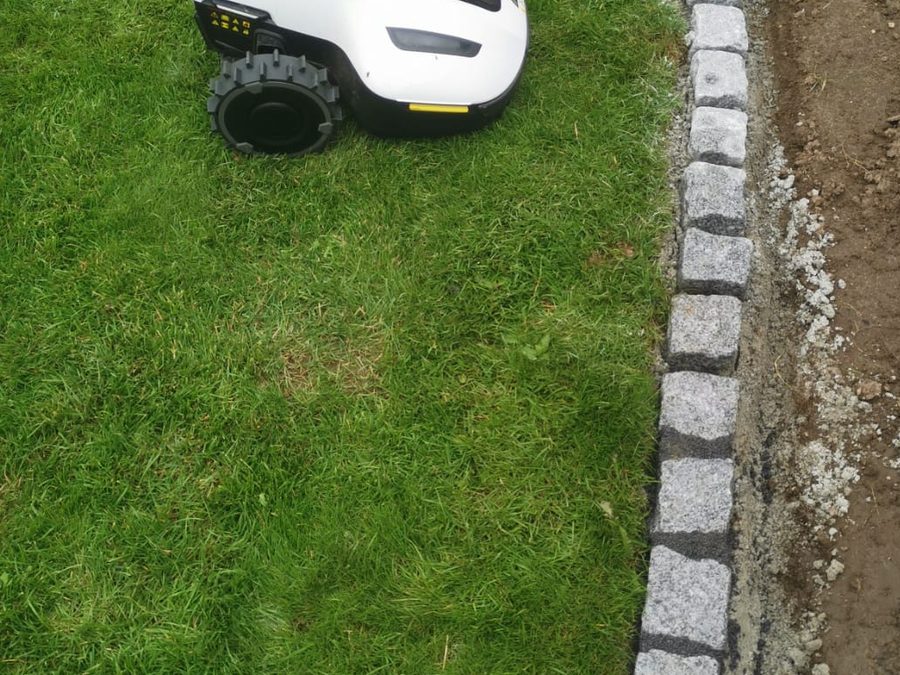 Mähroboter auf einer Rasenfläche neben neu gesetzter Granit-Bordkante